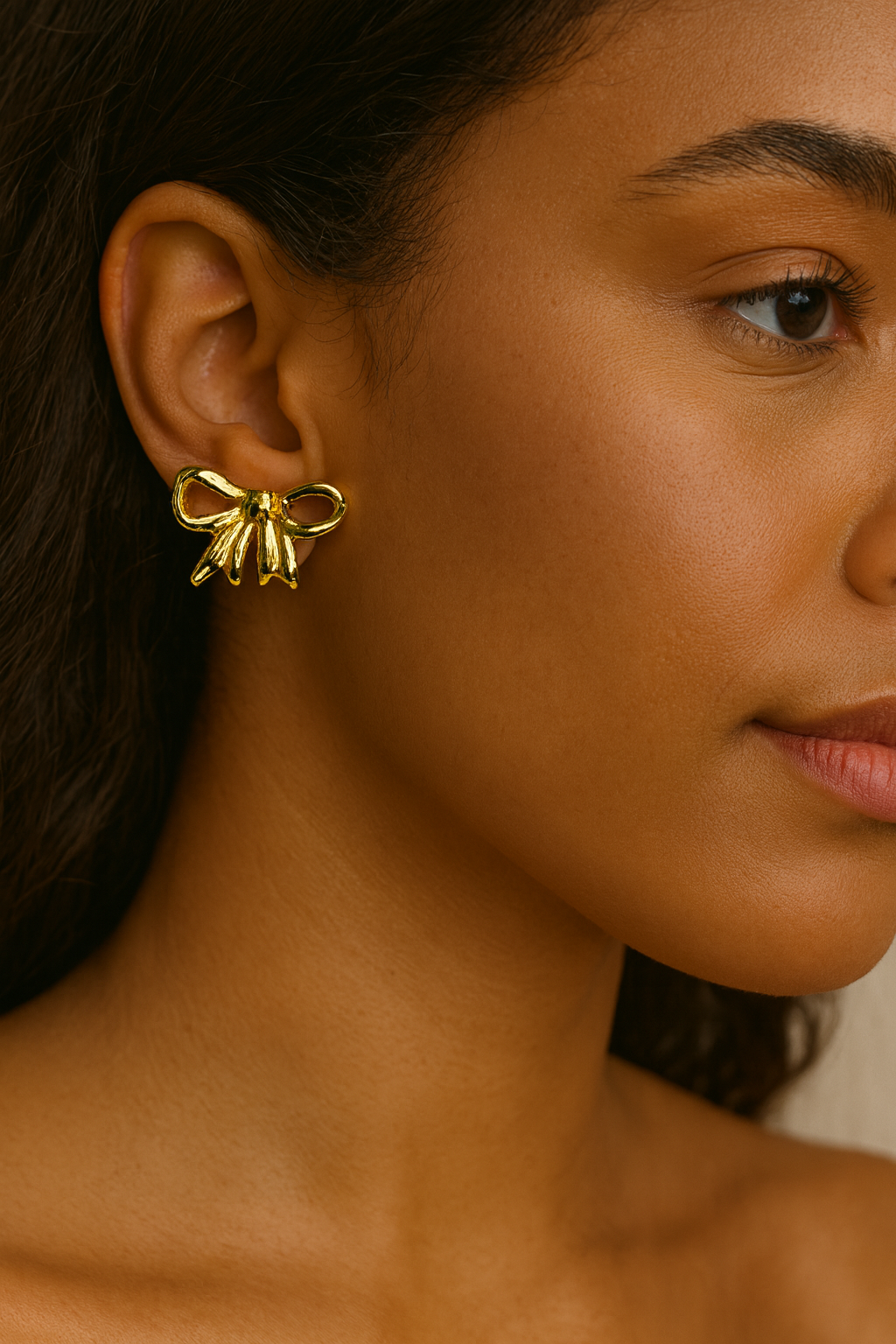 Close-up of a woman wearing a gold bow-shaped earring against a neutral background