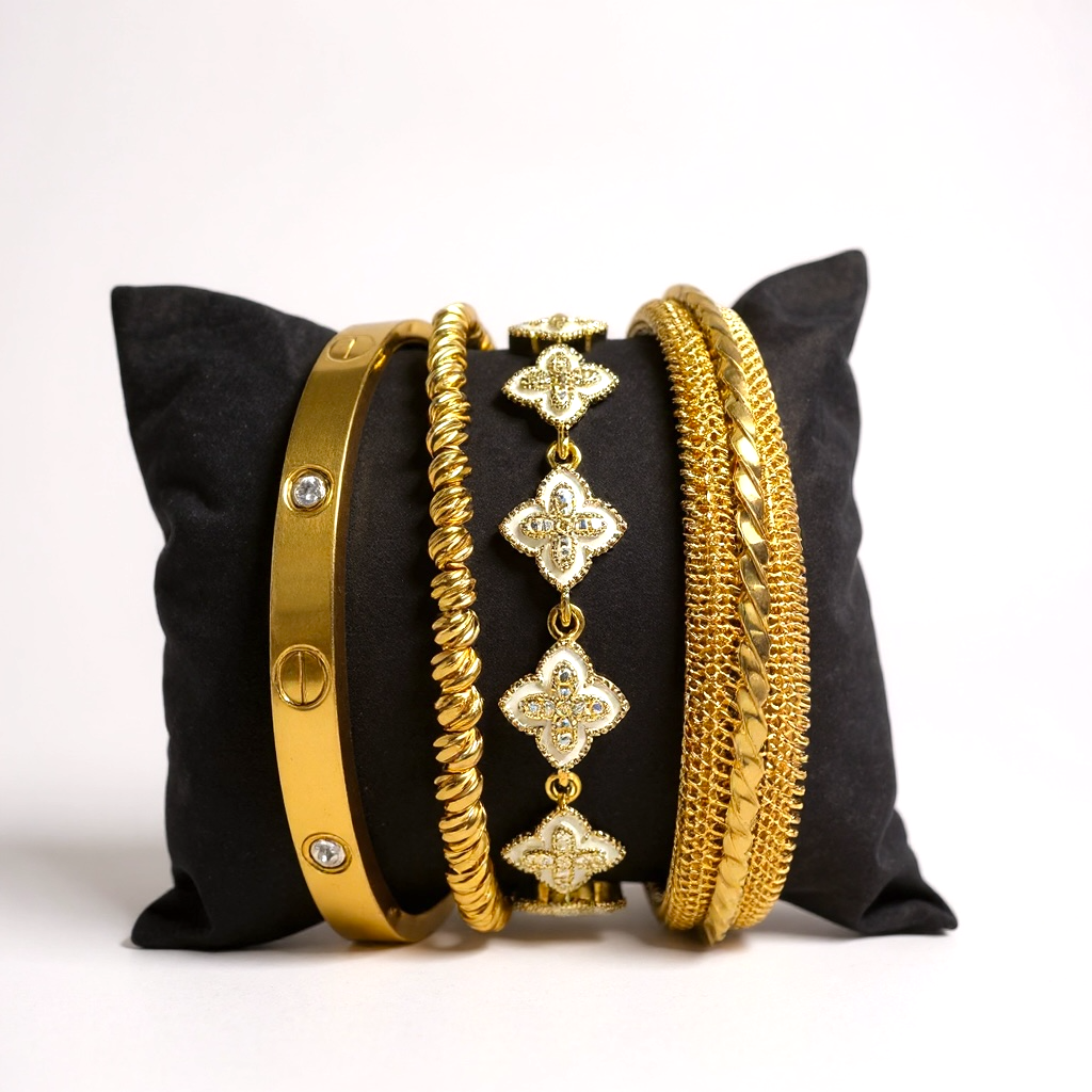 four gold bracelets on a black pillow with a white background