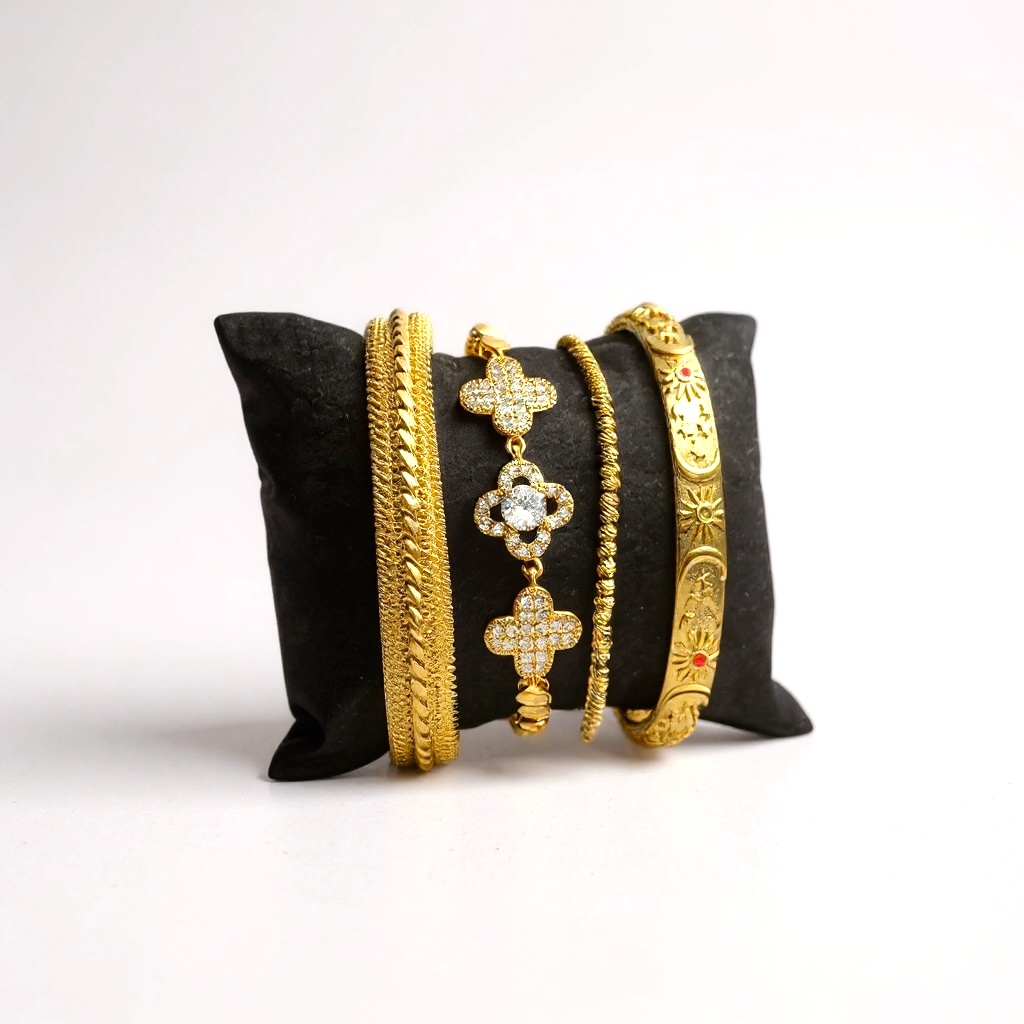 Set of 18k gold-plated bangles on a black pillow against a white background