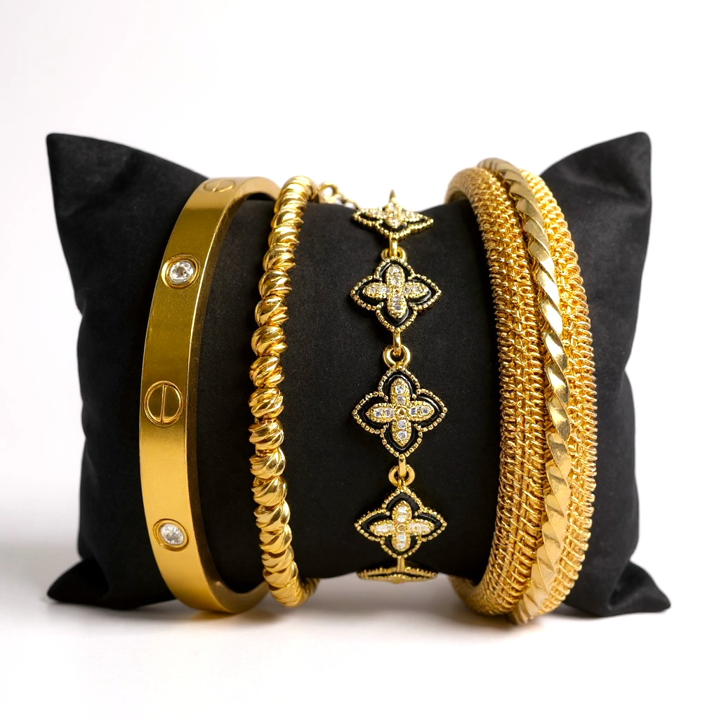 Gold bracelets on a black pillow with a white background