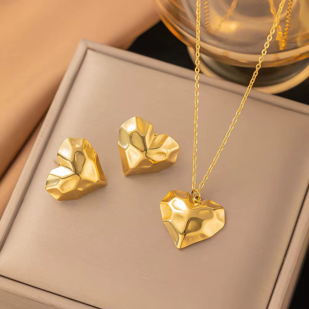 Gold heart-shaped jewelry set on a beige surface
