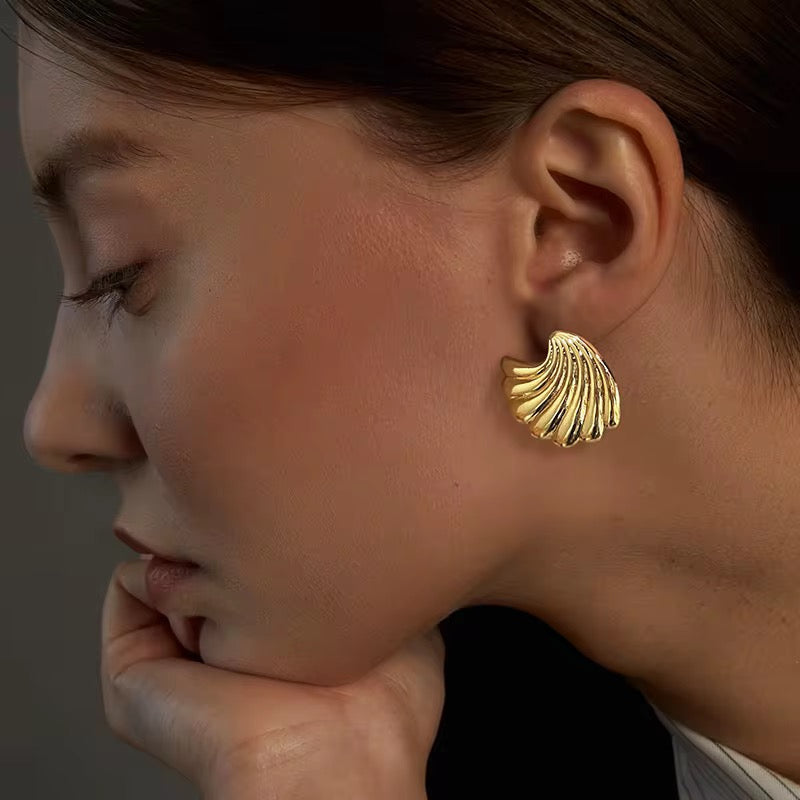 Close-up of a person wearing a gold shell-shaped earring against a neutral background
