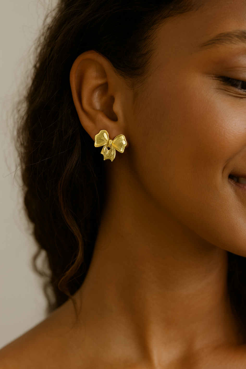 Close-up of a woman wearing gold bow-shaped earrings with a neutral background